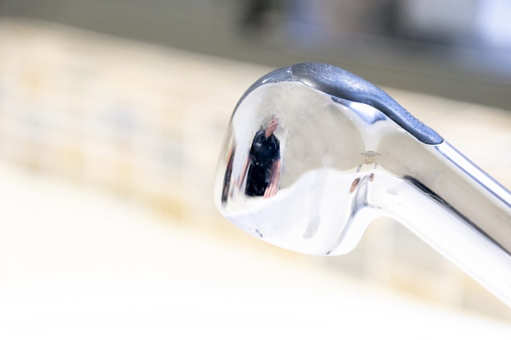 Detail of a chrome mixer tap, the plumber's dark shirt caught in the reflection